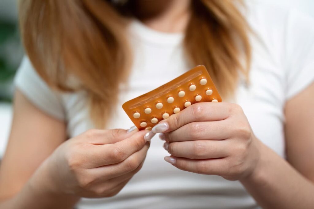 young woman looks down at her birth control pills