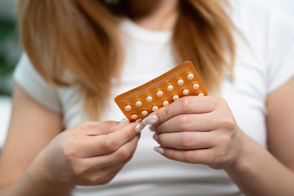 young woman looks down at her birth control pills